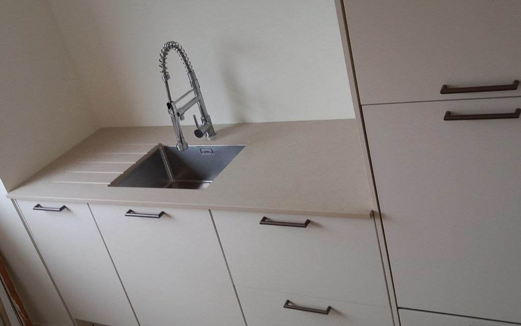 Évier moderne en acier inoxydable avec robinet à haute tige, intégré dans un comptoir clair avec des meubles de cuisine minimalistes.