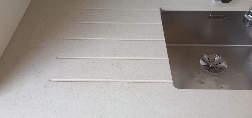 Vue d'un évier en inox intégré dans un plan de travail en surface claire avec des rainures.