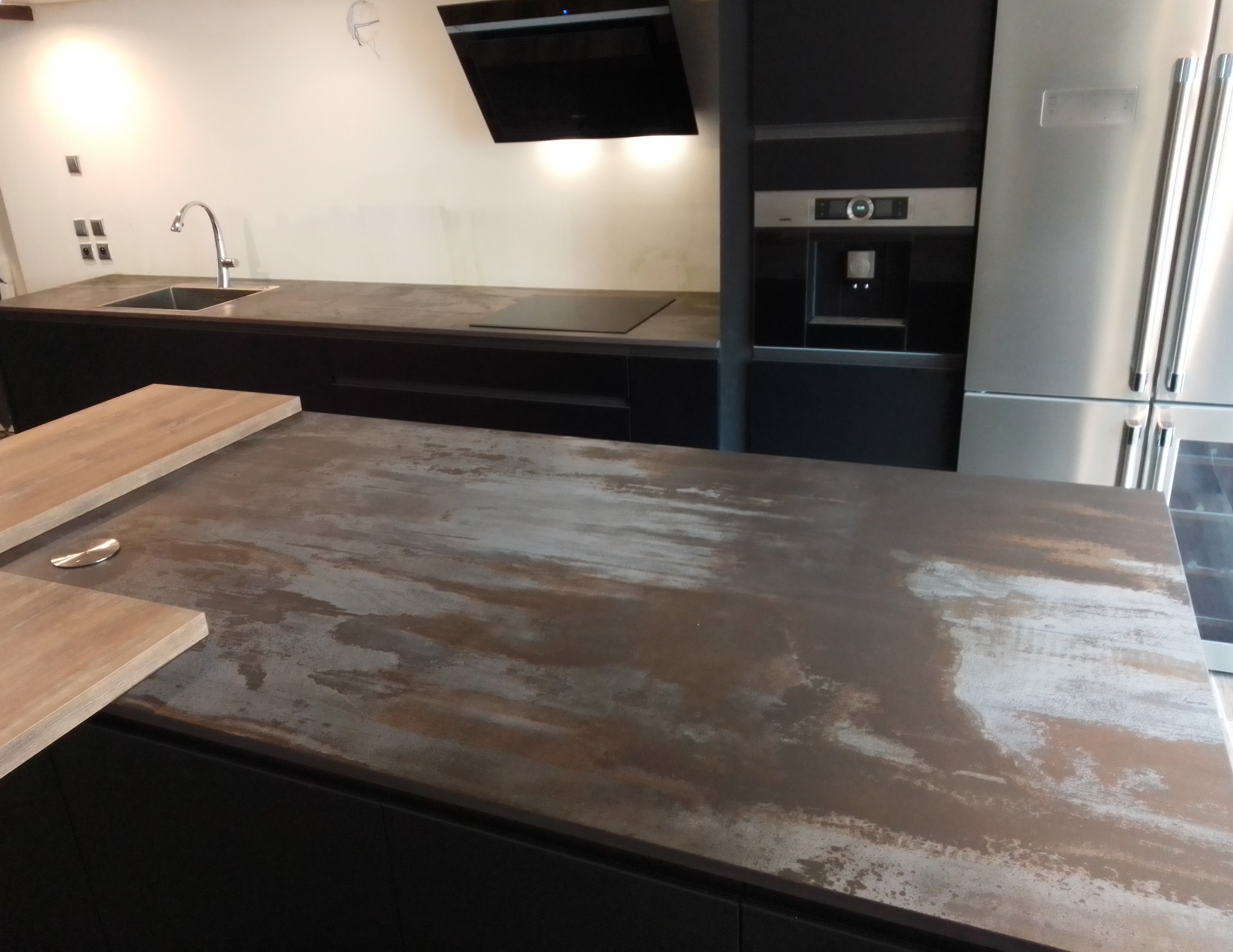 Cette cuisine affiche un style industriel et contemporain, mis en valeur par un plan de travail en Dekton Trillium aux nuances métalliques et oxydées. Son aspect brut, inspiré de l’acier vieilli, apporte du caractère et une véritable identité à l’ensemble de la pièce.